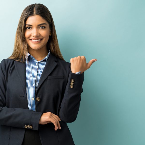 Hispanic female executive gesturing at copy space while making eye contact in studio