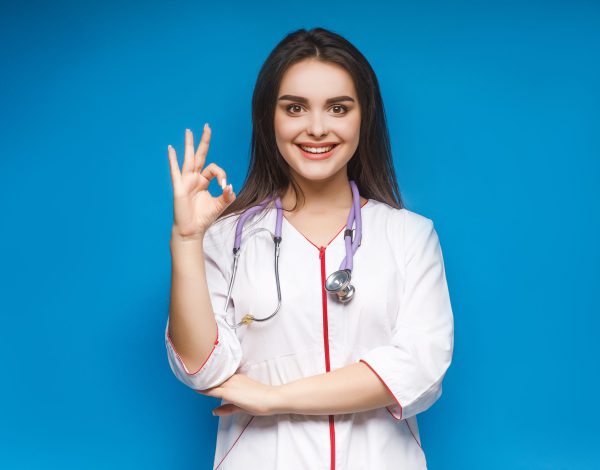 Photo of young female doctor make okaysign, over blue background.