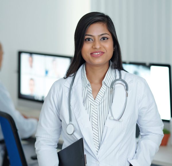 Positive young female physician standing in medical office with clipboard in hand ready to visit sick patients