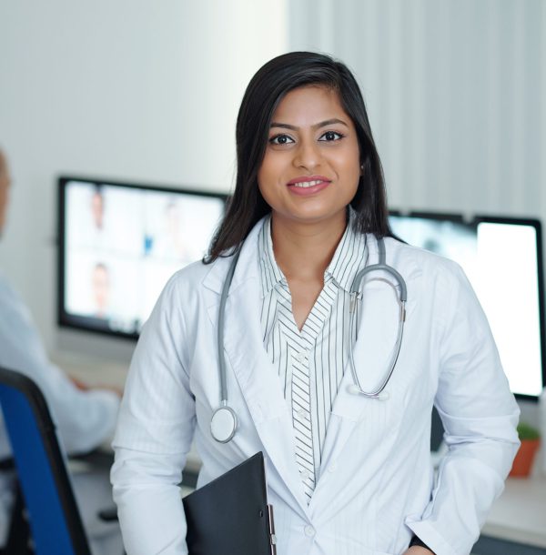 Positive young female physician standing in medical office with clipboard in hand ready to visit sick patients