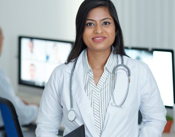 Positive young female physician standing in medical office with clipboard in hand ready to visit sick patients